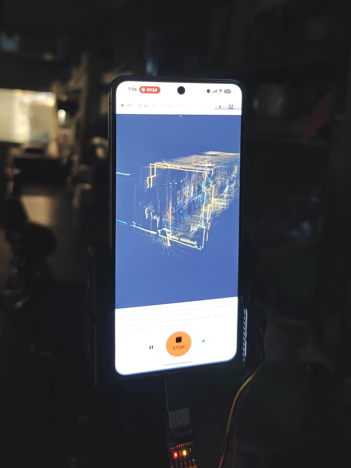 A phone on the rig, mid-scan in an unlit workshop — the point cloud building on its screen, the lidar puck's indicator lights below.